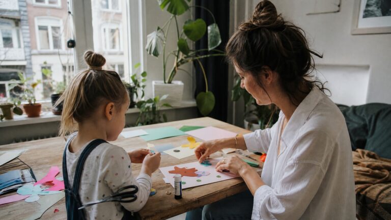 Mother and daughter making a paper collage craft together at home, connecting through creative play