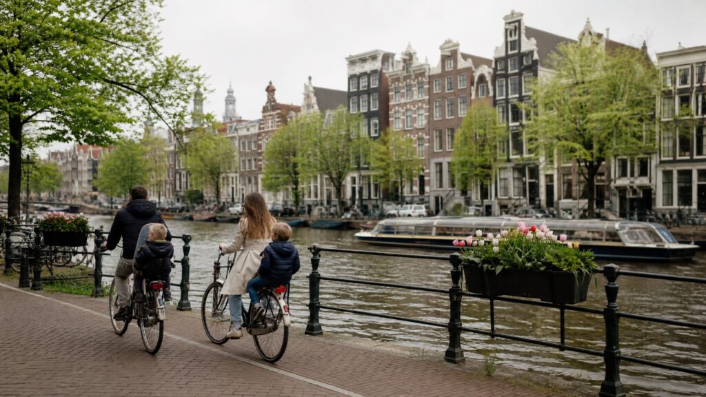 A family cycling along an Amsterdam canal, two small children on the back of the bikes
