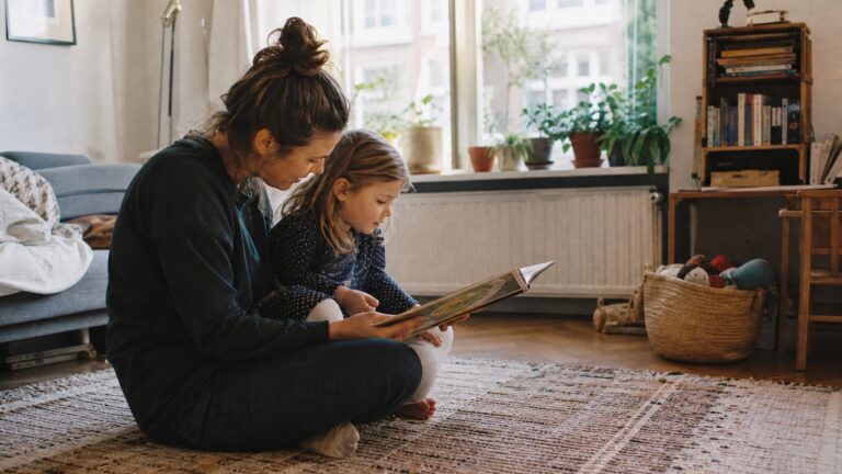 Mother reading a picture book with her young daughter at home, aware parenting coaching in Amsterdam