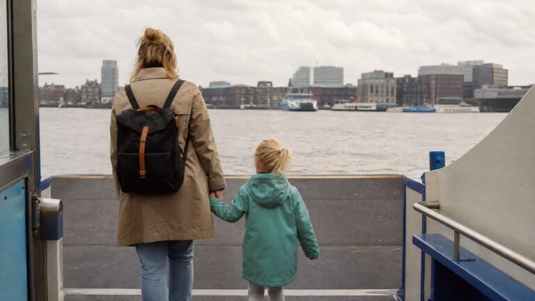 Parent and child holding hands boarding the free Amsterdam ferry across the IJ with the city skyline in the background