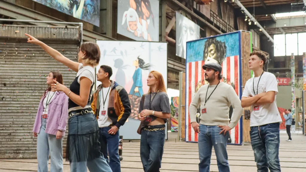 A guide points up at a large painted canvas while a small tour group looks on inside the STRAAT Museum warehouse