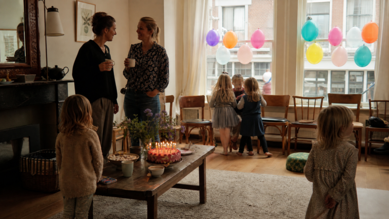 Dutch kids birthday party traditions, children and parents in a living room circle of chairs with cake and balloons