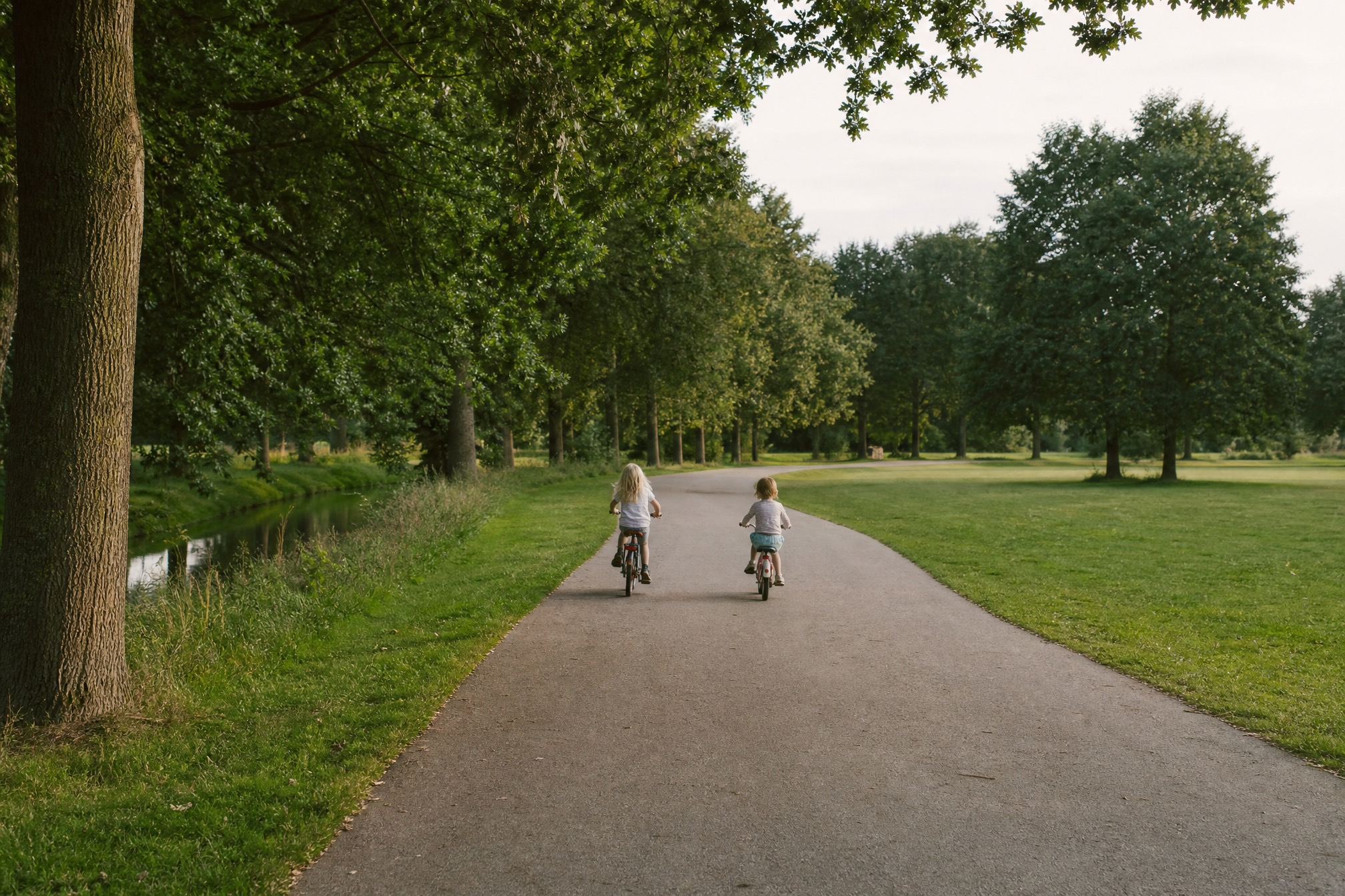 Two children cycling along a path in a Dutch park, learning to ride