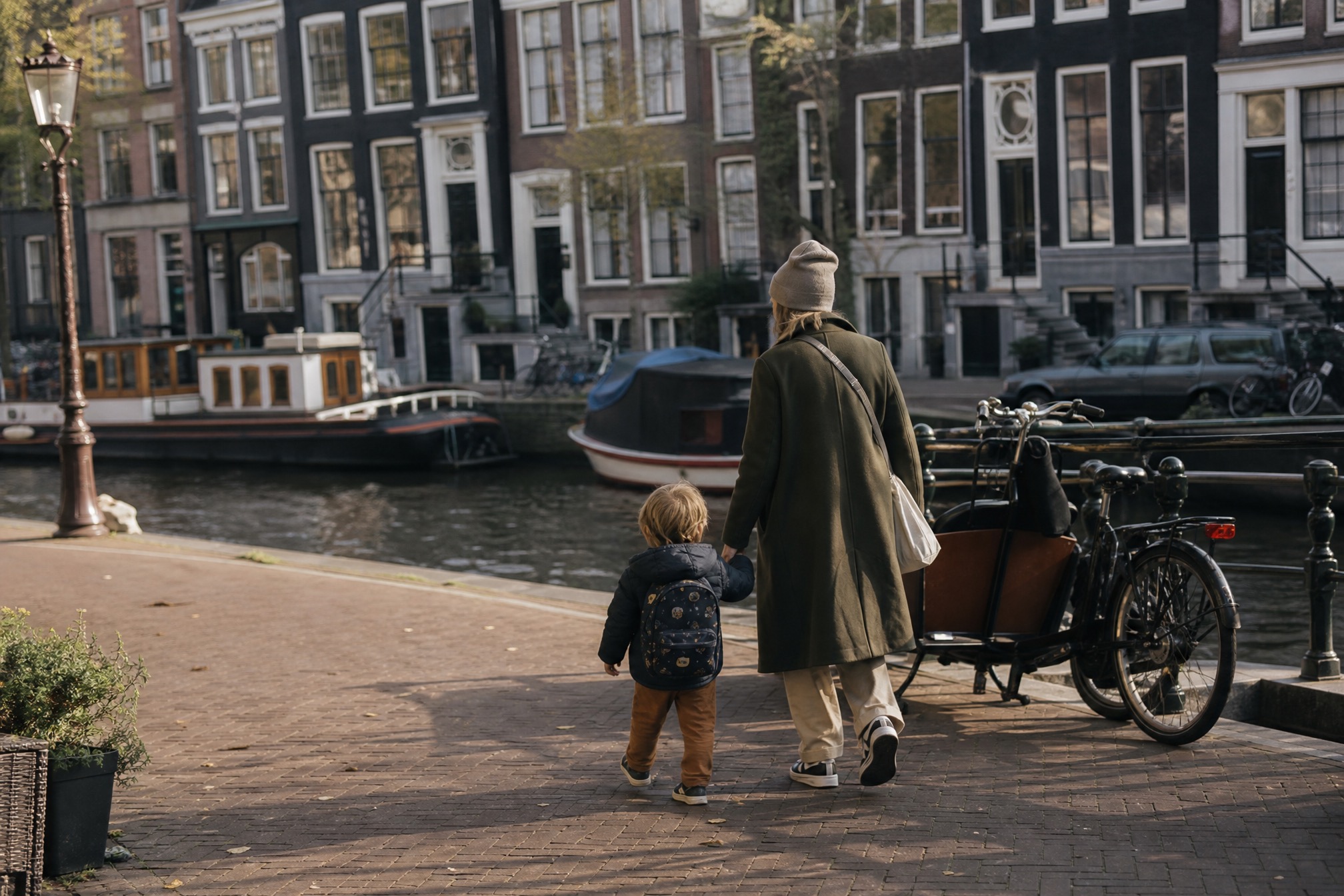 Parent and toddler walking beside an Amsterdam canal near a cargo bike, the kind of open water Dutch swim diplomas are designed for