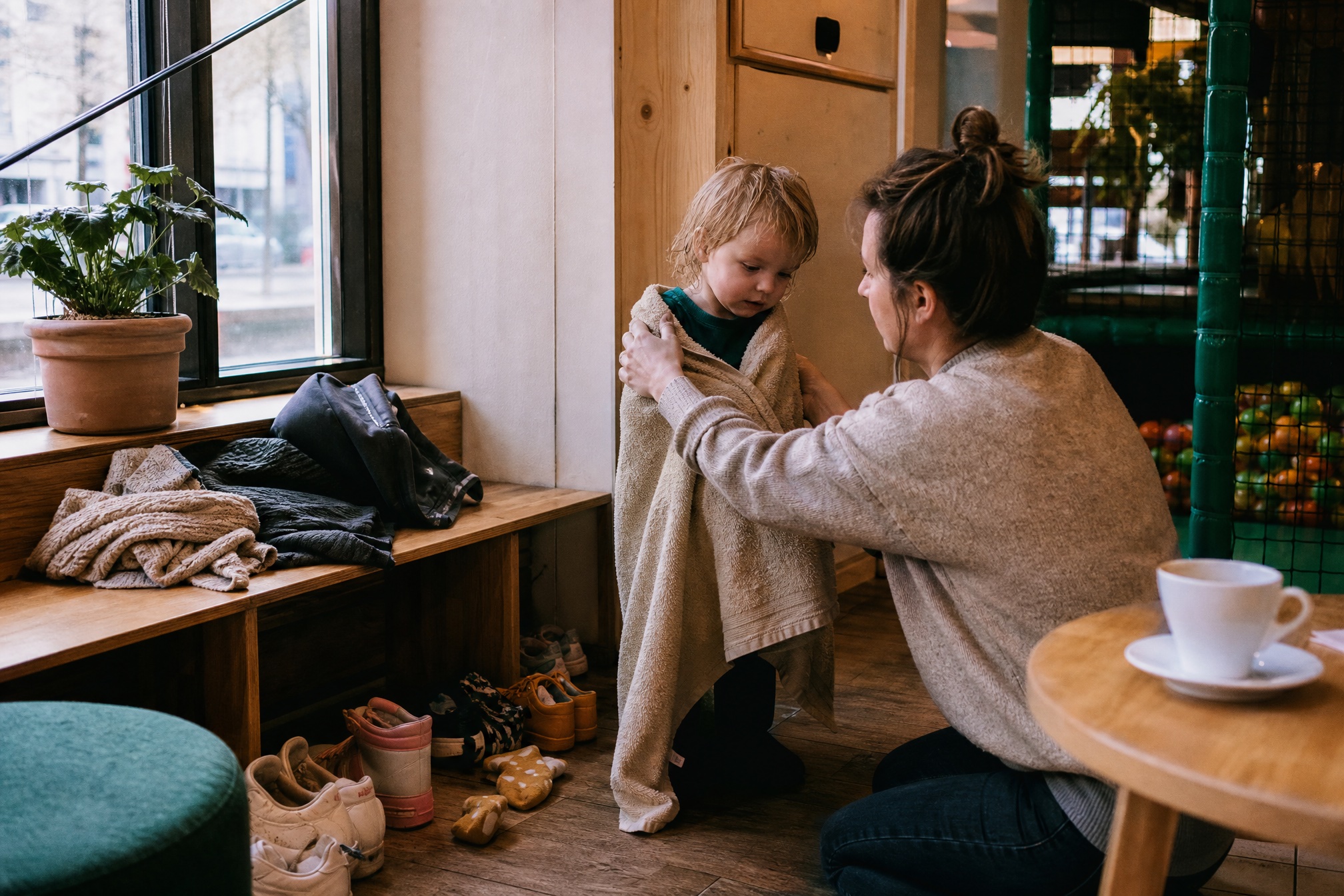 Parent drying off a toddler after soft play at an indoor playground cafe corner