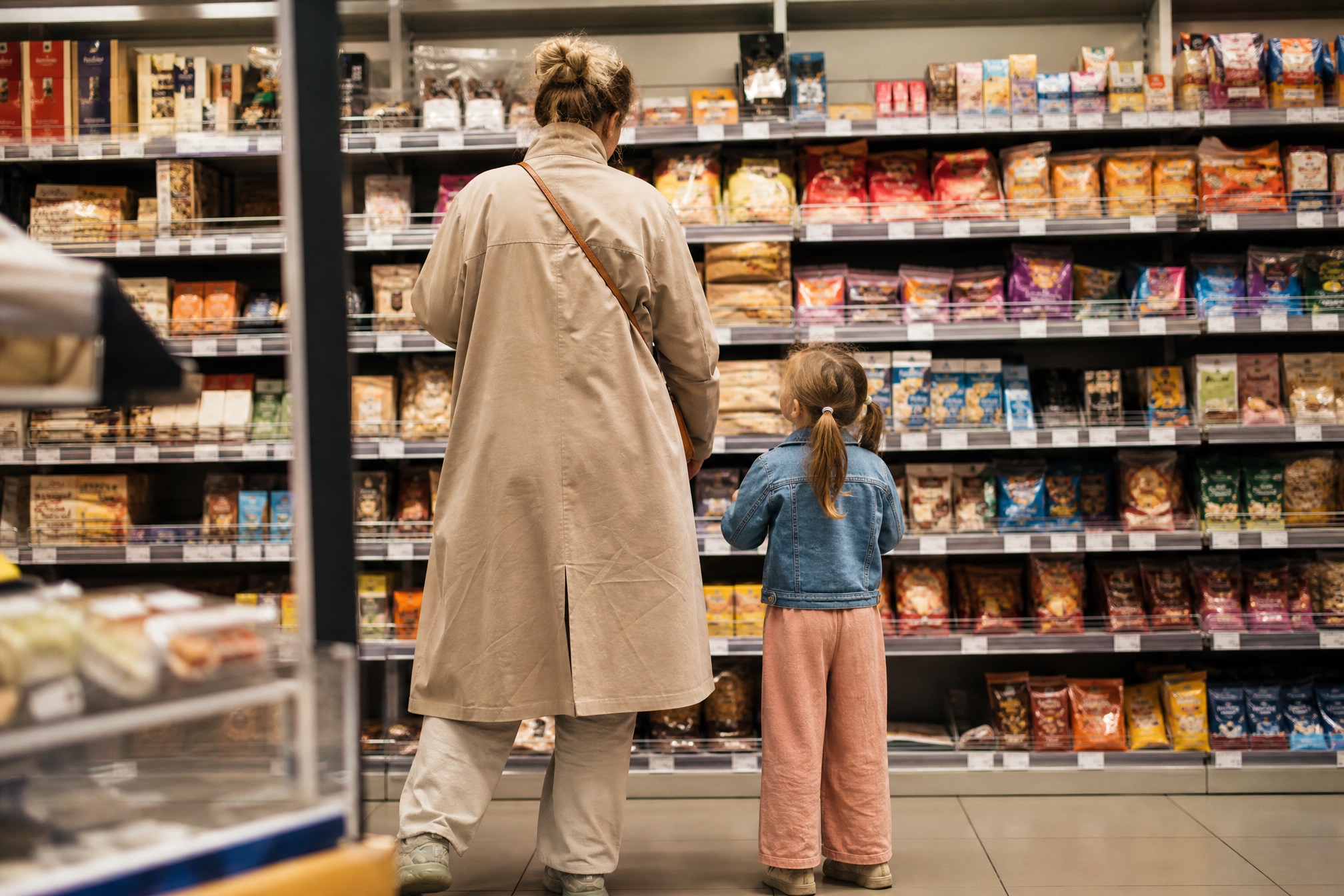 Parent and child choosing packaged snacks in a Dutch supermarket for a school birthday treat