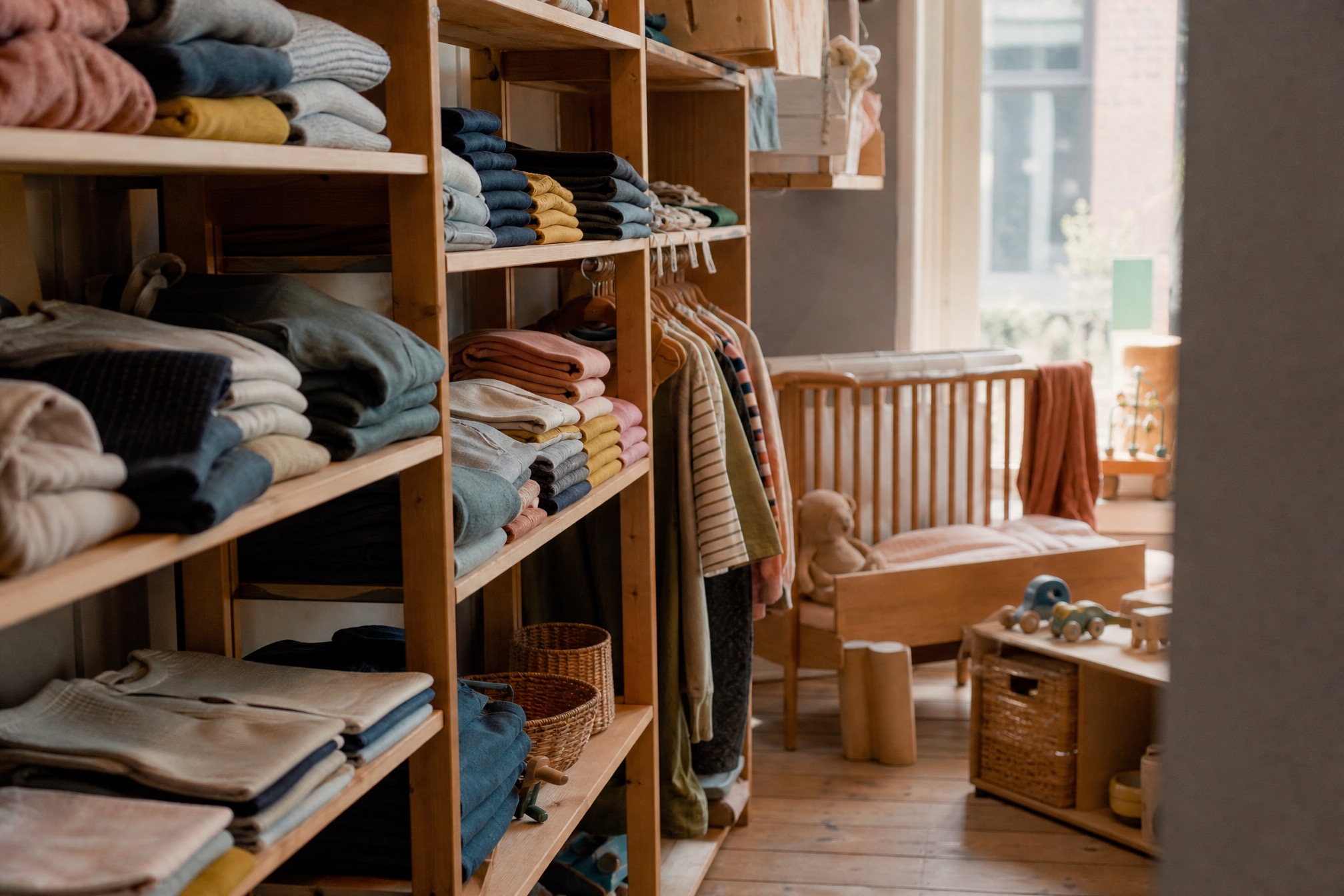 Secondhand childrens shop with folded kids clothes on wooden shelves and a wooden cot