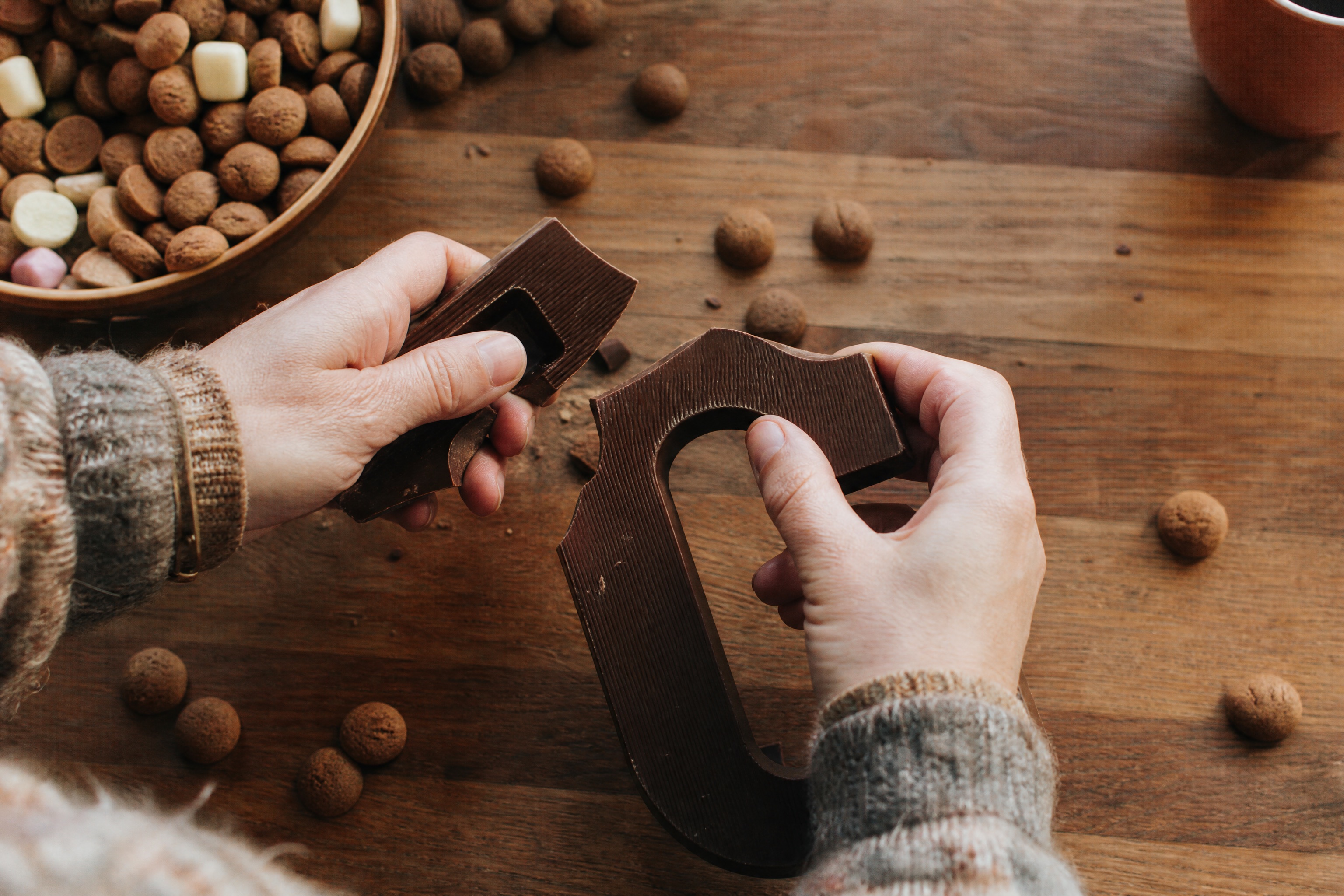 Hands breaking a Sinterklaas chocolate letter over a table of pepernoten