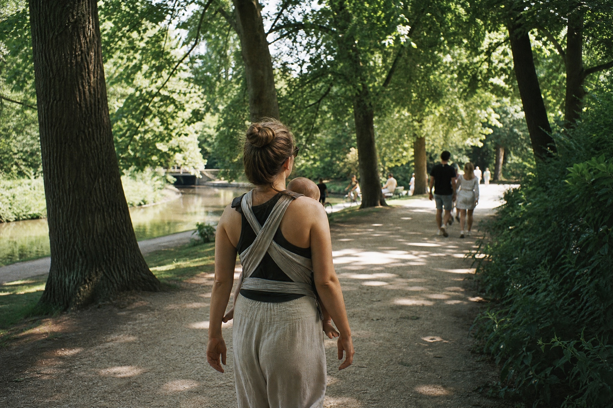 Parent walking a shaded Vondelpark path in Amsterdam with baby in a carrier