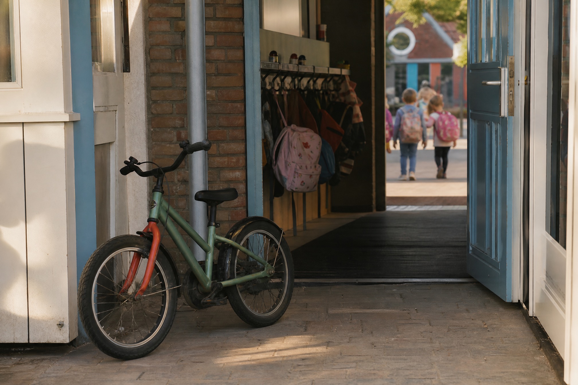 Child bicycle parked outside a Dutch primary school entrance with backpacks on hooks