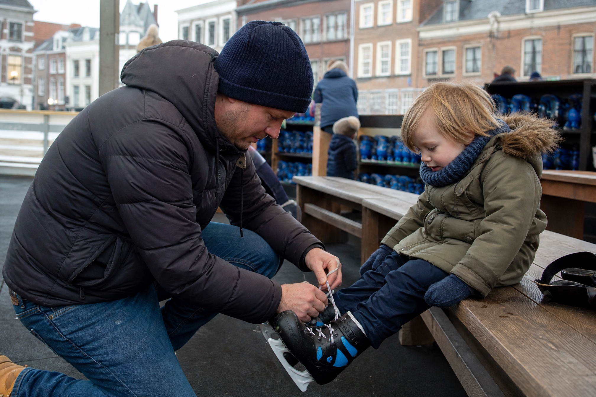 A parent helps a child lace up ice skates at the Winter Village Amstelveen rink