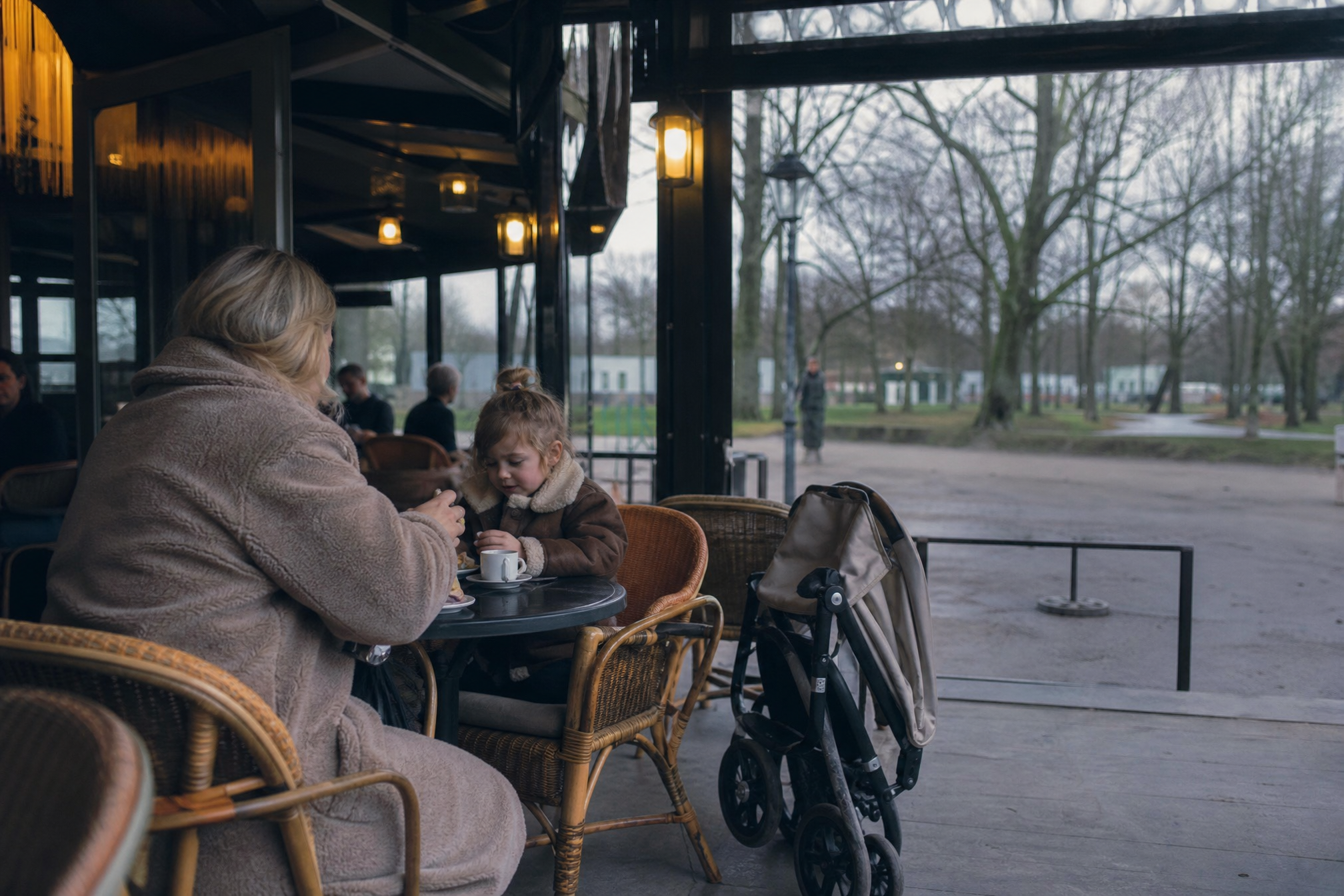Parent and child at a cozy cafe terrace with a folded buggy nearby on a cold winter afternoon